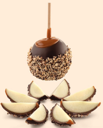 Une pomme au caramel trempée dans du chocolat et des noix, planant au-dessus de tranches de pomme au caramel du même type.