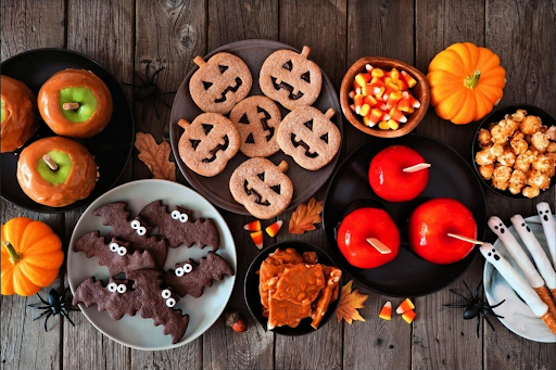 A variety of colourful homemade Halloween treats including candy apples, bat brownies, and pumpkin cookies.