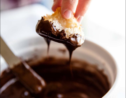 Coconut macaroon being dipped in melted chocolate. Le macaron à la noix de coco trempé dans du chocolat fondu