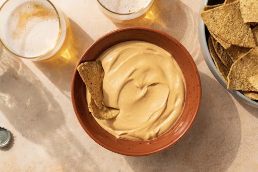 Vegan nacho dip in a terracotta bowl with a chip. Nacho vegan tremper dans un bol en terre cuite avec une puce