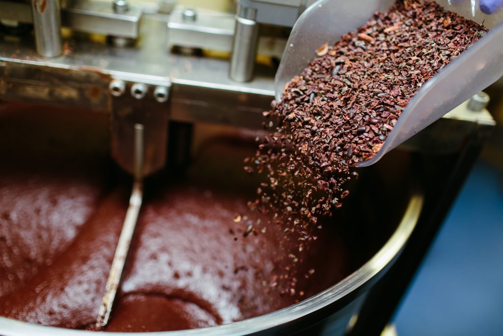 The process of chocolate making shown through cocoa nibs sprinkled into a cocoa grinding machine. Le processus de fabrication du chocolat montré à travers les nibs de cacao saupoudrés dans une machine à broyer le cacao.