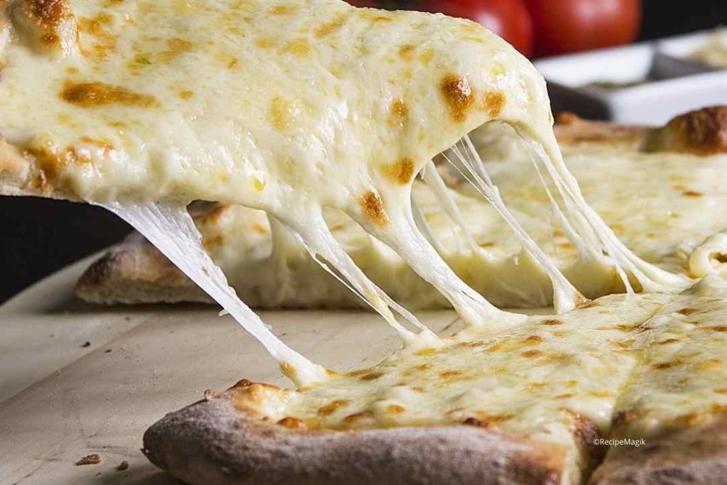 A closeup of pizza, emphasizing the stretchiness of the vegan mozzarella. Un gros plan de pizza, soulignant l’étirement de la mozzarella végétalienne