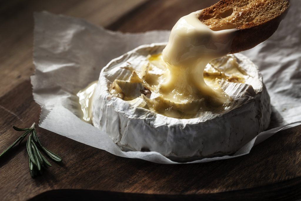 A piece of bread being dipped in melted Camembert Cheese