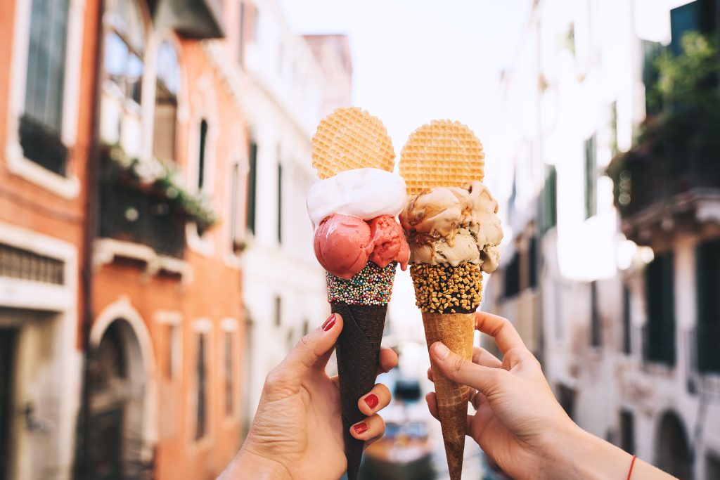 Beautiful and delicious italian gelato in waffle cone in front of streets and bridges of Venice. Ice cream in girls hands on background of water canal and historic buildings of Italy. Travel Europe.