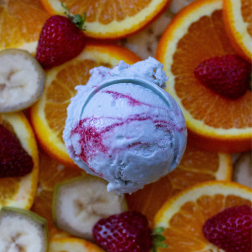 Une boule de glace blanche à la banane avec un tourbillon rose sur des bananes, des fraises et des oranges fraîches.