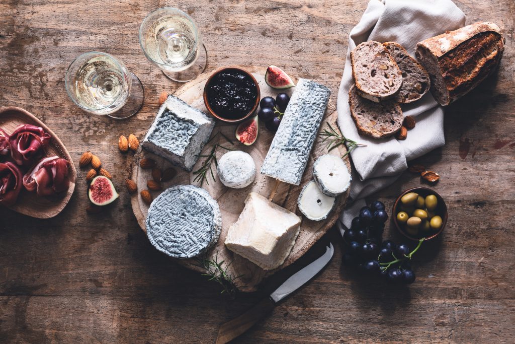 Un plateau en bois avec une variété de fromages de chèvre, du pain et du vin autour.