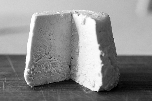 A tall block of white crumbly cornilly goat cheese with a slice cut out.