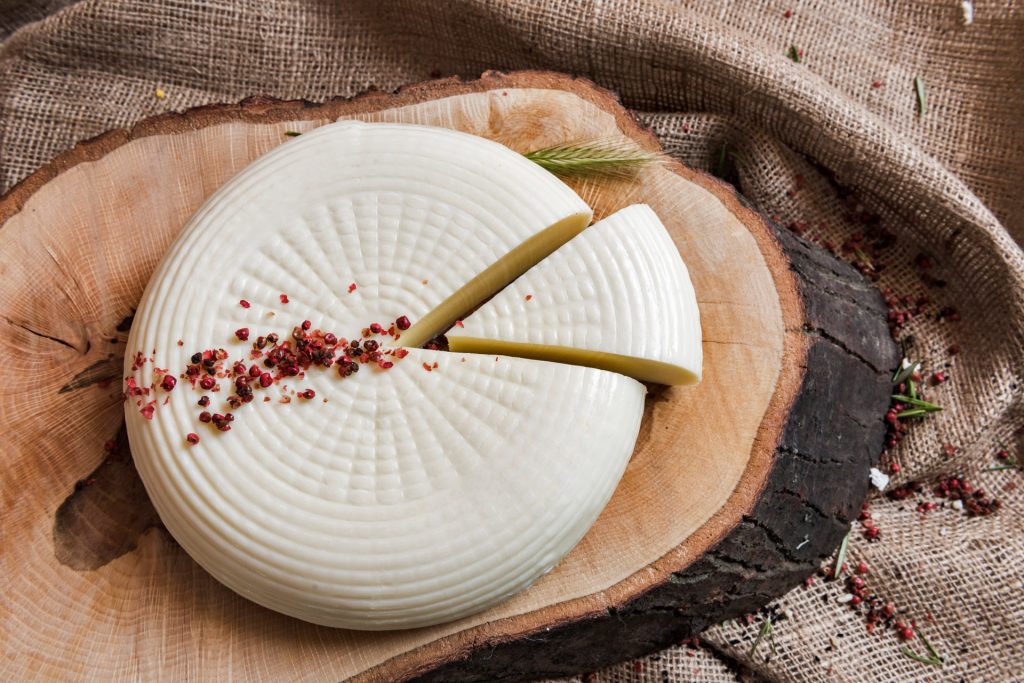 A round of sepet cheese with a piece sliced and red peppercorn on top.