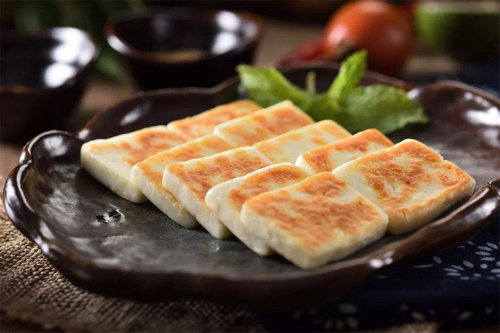 5 slices of golden Yunnan goat Cheese on a brown ceramic plate.